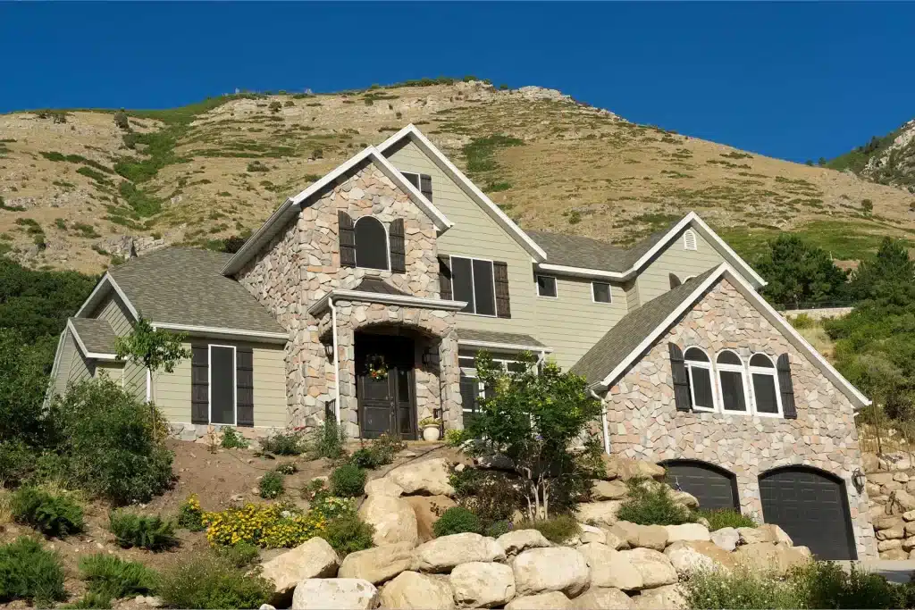 home on a hill with stone base, two black garages, various plants and decorative stones